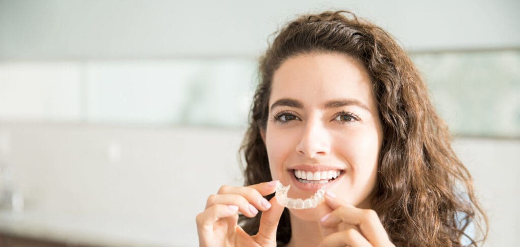 Portrait Of Beautiful Patient Holding Orthodontic Retainers In Dental Clinic