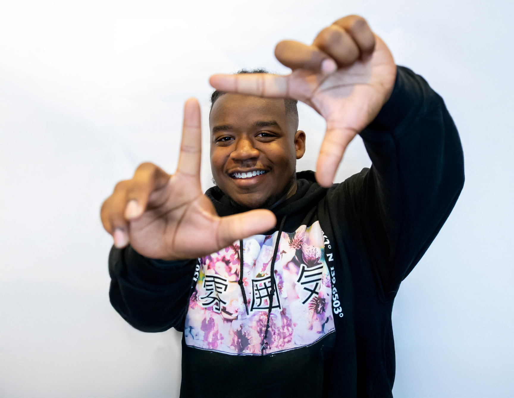 A Man Framing His Smile With His Thumb And Index Fingers
